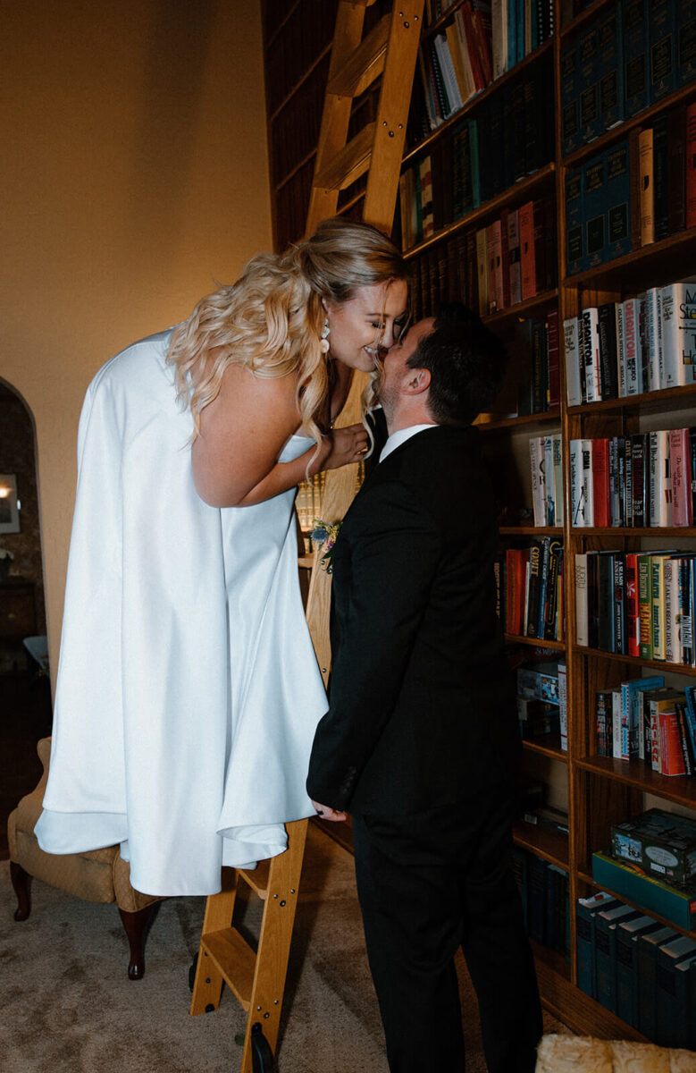 bride stands on a ladder and kisses the groom