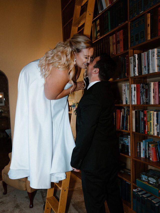 bride stands on a ladder and kisses the groom